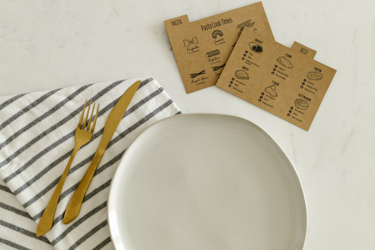 Top view of a ceramic plate with gold cutlery, striped napkin, and recipe cards on a marble table.